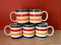 Front view of five Hudson's Bay stripe mugs stacked with handles facing outward.