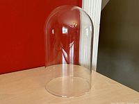 Clear glass dome displayed on red background, showing its overall shape and transparency.