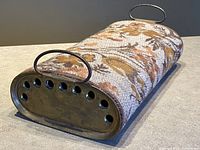 Side angle view of foot warmer showing floral fabric exterior and metal handles.