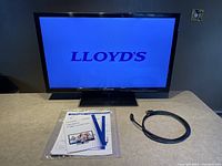 Photo of Lloyd's 29-inch LED TV powered on showing Lloyd's logo on screen along with HDMI cord and user manual on table.