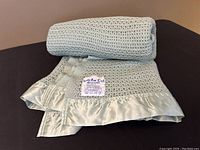 Rolled and partially folded green Lan Air Cel wool blanket with satin trim, showing texture and knit pattern.