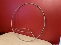 Front view of the brass circular plant hanger on a beige surface against a red wall.