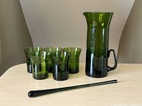 Set showing pitcher, five glasses, and stirrer on table from front angle