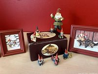 Eight gnome figurines displayed around a brown box and four small red wood frames against red wall