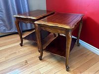 Pair of vintage Hammary wood side tables with scalloped edges and curved legs, placed on a hardwood floor against a red wall.