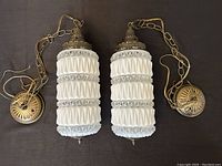 Pair of vintage RD Dero white accordion-style textured pendant ceiling lights with brass ornate fixtures and chains, laid flat on dark surface.