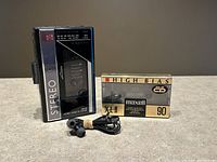 Front view of Sanyo MGR59 cassette player with Maxell cassette tape and black wired earbuds arranged in front.