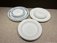 Two stacks of vintage Corelle plates and bowls arranged side by side, Old Town Blue patterned plates on the left stack and solid white plates and bowls on the right.