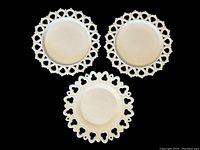 Overhead view of three vintage milk glass plates: two with teardrop lace edge and one with shell and club lace edge.