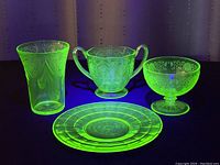 Four-piece vintage uranium green glass dish set under blacklight showing bright green fluorescence.
