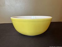 Side view of vintage Pyrex bowl showing yellow exterior and white interior with smooth finish and light wear.