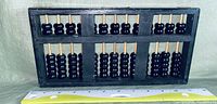 Photo of full abacus showing black rounded beads on bamboo rods within a wooden frame, with a measuring ruler showing size approximately 23 cm wide.
