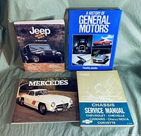 Four automotive books arranged on a green fabric background: Jeep book, A History of General Motors, Mercedes book, and 1969 Chevrolet Chassis Service Manual.