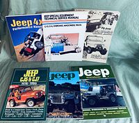 Photo of six Jeep automotive books and manuals spread out for display on a green background showing front covers clearly including various technical service and model guides.