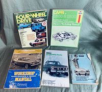 Lot of 5 automotive books arranged on a fabric surface. Titles visible: Four-Wheel Drive Magazine, Capri V6 Workshop Manual by Haynes, Capri 2000 Maintenance Manual by Drake, Off-Roading Guide, and Skoda Owner's Manual.