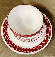 Top view of stacked bowls and plates showing red geometric quatrefoil pattern on white Corelle dinnerware.