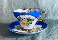 Side view of the porcelain cup and saucer showing the yellow rose design, blue band, and gold handle.