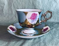 Side view of the porcelain cup and saucer showing pink rose decorations and gold trim