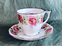 Side view of porcelain cup and saucer set showing pink rose design and gold trim.