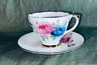 Side view of porcelain cup showing pink and blue floral pattern with gold trim on handle and rim.