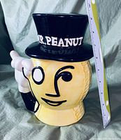 Front and side view of the Mr. Peanut cookie jar with a measuring tape for scale, showing detailed features and top hat with "MR. PEANUT" text.