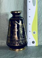Front view of the small black vase with gold classical figures and ruler showing height approximately 4.5 inches.