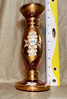 Front view of small reddish-brown glass vase with white and pink floral decoration, gold accents, and a measuring tape showing approx 7 inches in height