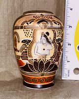 Front view of the small vase showing a seated human figure with a headdress in detailed Asian-style painting.