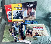 Photo shows a group of approximately 14 horse racing magazines and programs. Includes multiple issues of Thoroughbred Record magazine with different cover colors (red, yellow, brown) featuring racehorses and jockeys.