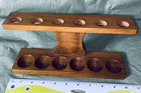 Angled side view showing wooden pipe stand with two horizontal bars with six pipe holders each, vertical central support and a ruler for scale.