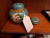 Photo of 2 cloisonne pieces: a ginger jar with floral designs and a small round trinket box with a dragonfly on its lid.