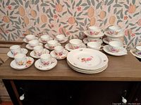 Wide view of the entire 36-piece KPM porcelain dinnerware set including plates, cups, and saucers all displaying varied floral and butterfly designs.