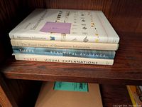 Four Edward Tufte books stacked on wooden shelf: Envisioning Information, The Visual Display of Quantitative Information, Beautiful Evidence, Visual Explanations.