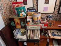 General view showing assortment of decorative and advertising tins, various shapes and designs, stacked and arranged.