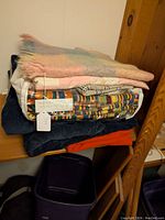 Stack of blankets and bedspreads showing multiple items piled including blue corduroy, multicolor Kente cloth, and pink baby quilt.