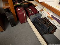 Photo showing burgundy suitcases, light blue suitcase, and two black and brown suitcases under a mirrored wall with labeled sheets.