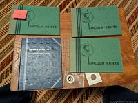 Four vintage green and blue Lincoln Cent collector albums laid out flat with two loose coins in flips