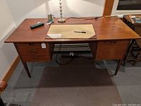 Full view of the teak desk showing flat top surface, drawers on left, legs, and overall structure.