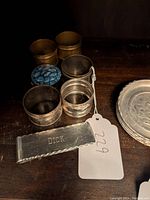 Photo showing group of napkin rings and metal pieces including rectangular piece engraved with 'DICK'.