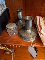 Two sterling weighted candlesticks displayed with a small dresser jar on a wooden shelf.
