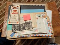 Top view of a box with assorted envelopes, postcards, and a booklet titled 'Save For Defense' containing Defense Stamps
