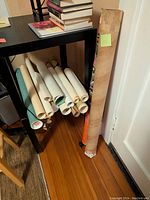 Rolled posters and tubes stored horizontally under a table and one vertical in a cardboard tube at the floor corner