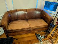Front perspective view showing full sofa with armrests and backrest in brown leather upholstery on wooden floor.