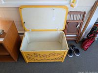 Open view of the vintage wooden toy chest showing the painted yellow exterior with brown floral designs and plain white interior.