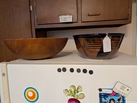 Photo showing the large wooden bowl next to the glazed pottery bowl, displayed on top of a fridge