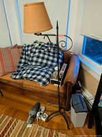 Full view of wrought iron floor lamp with brown fabric shade and curled decorative arm, positioned next to a couch in a living room.