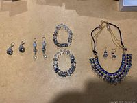 Photo showing four pairs of earrings, two beaded stretch bracelets, and a necklace with matching earrings featuring blue stones.