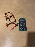 Digital multimeter with red and black probes coiled beside it on a flat surface, showing overall size and appearance