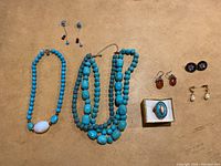 Top-down photo of assortment of costume jewelry items including blue bead necklaces, multiple pairs of earrings, and a turquoise stone ring.