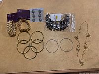 Top-down view of all jewelry items laid on a beige surface: cuff bracelets, bangles, a necklace with leaf charms, and earrings.